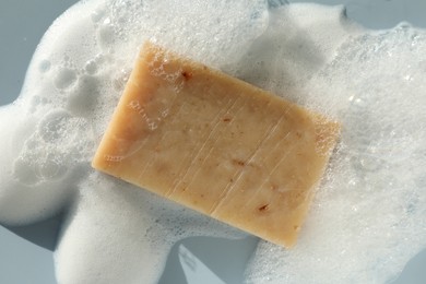 Photo of Soap bar with foam on grayish blue background, top view