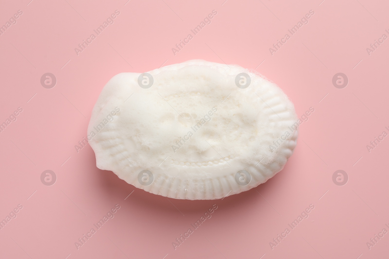 Photo of Soap bar with foam on light pink background, top view