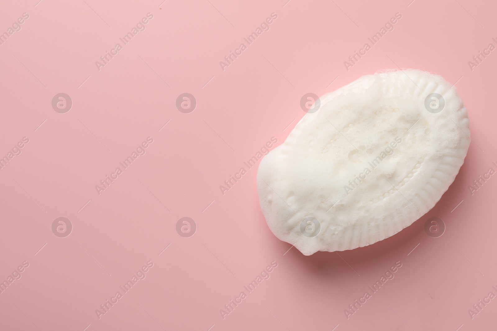 Photo of Soap bar with foam on light pink background, top view. Space for text