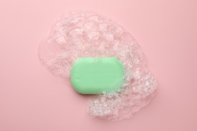 Photo of Soap bar with foam on light pink background, top view