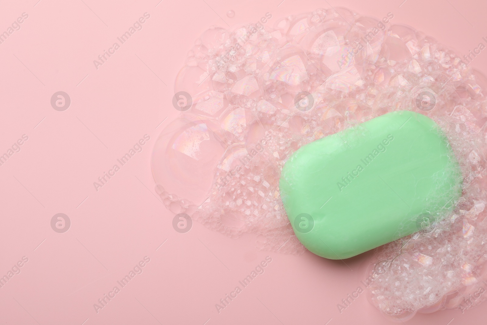 Photo of Soap bar with foam on light pink background, top view. Space for text