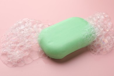 Photo of Soap bar with foam on light pink background, closeup