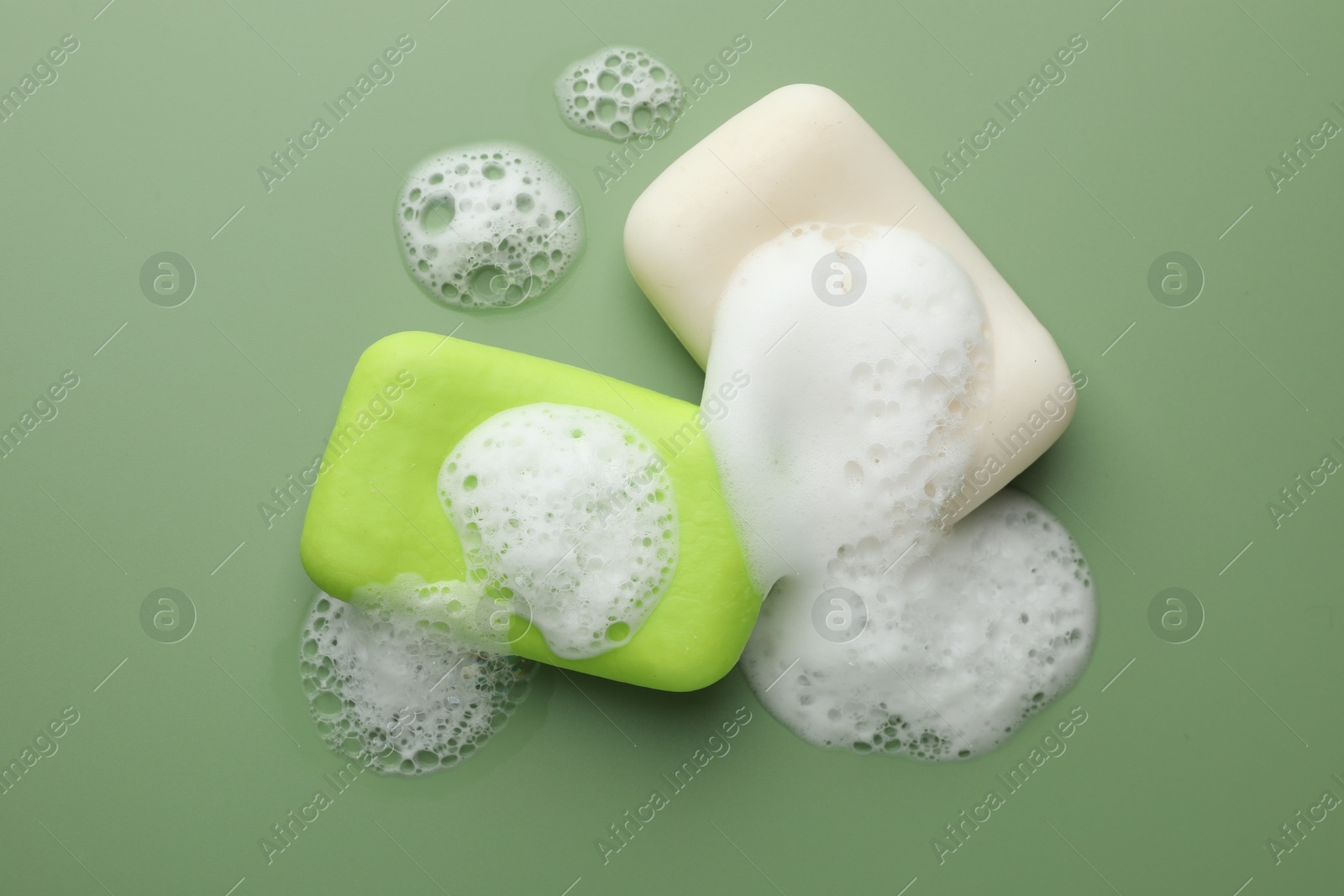 Photo of Soap bars with foam on green background, flat lay