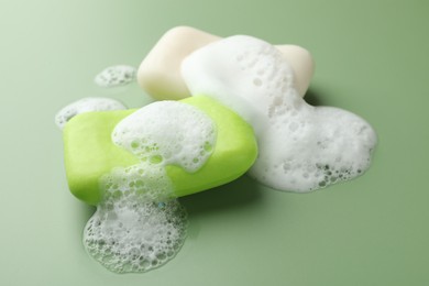 Photo of Soap bars with foam on green background, closeup