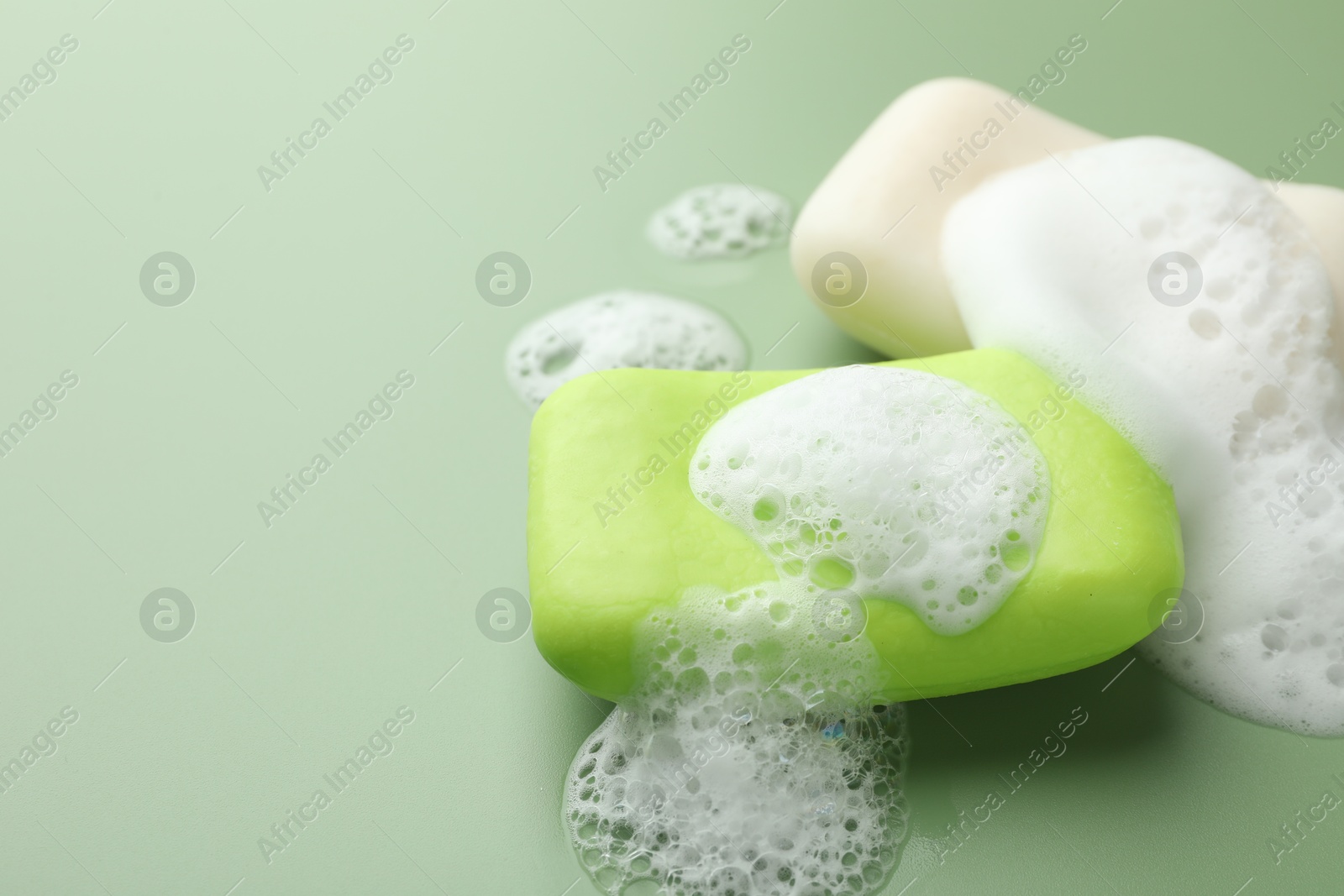 Photo of Soap bars with foam on green background, closeup. Space for text