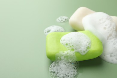 Photo of Soap bars with foam on green background, closeup. Space for text