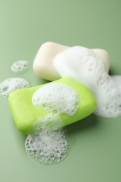 Photo of Soap bars with foam on green background, closeup