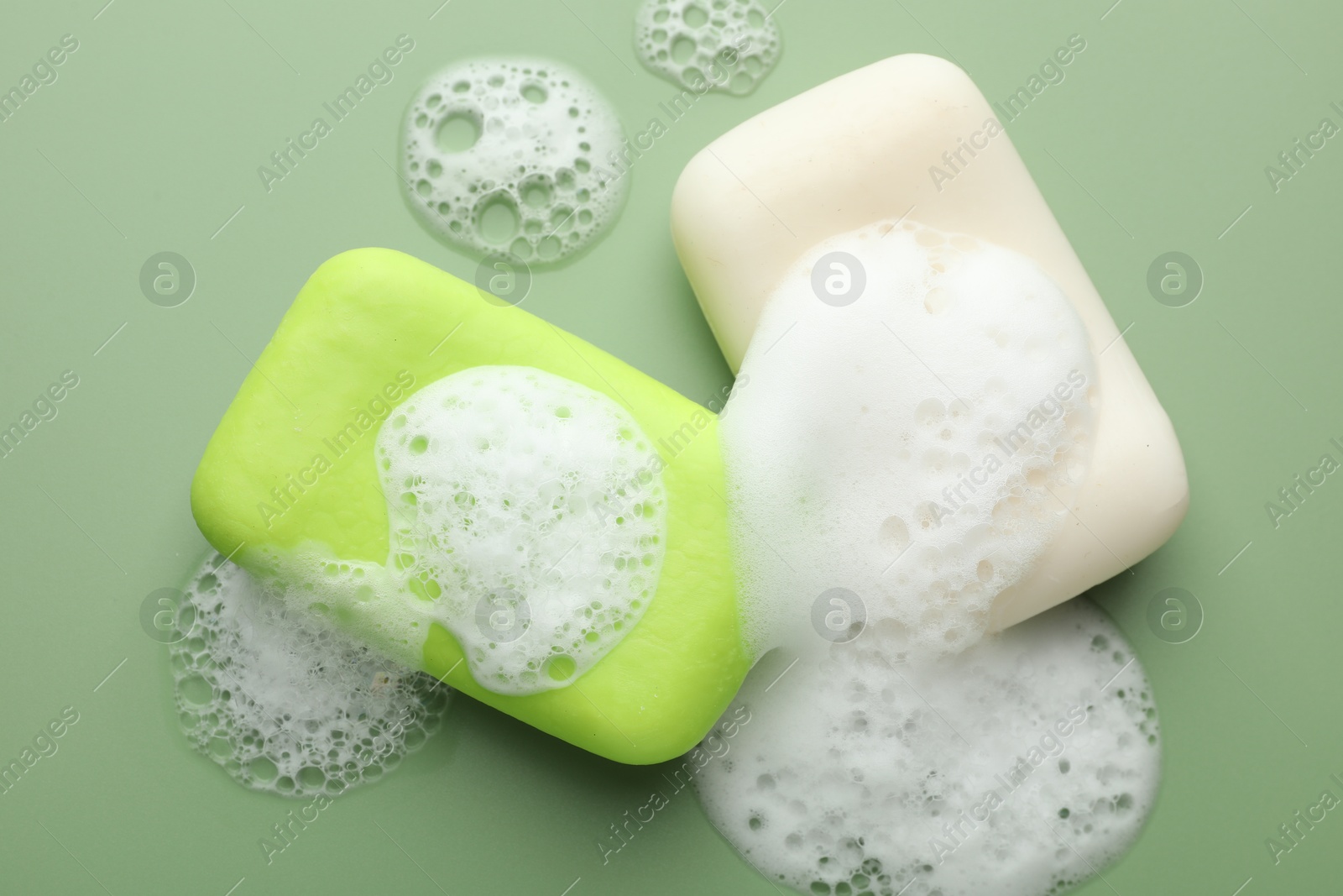 Photo of Soap bars with foam on green background, flat lay