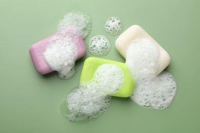 Photo of Soap bars with foam on green background, flat lay