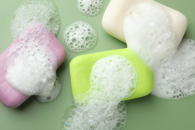 Photo of Soap bars with foam on green background, flat lay