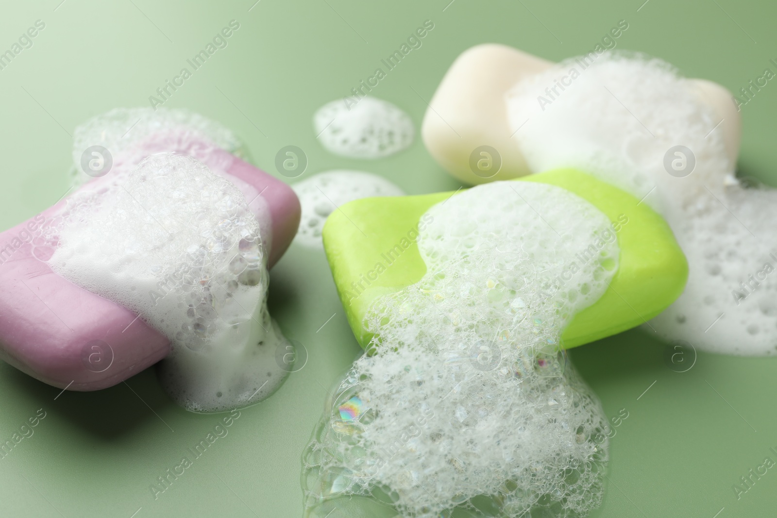 Photo of Soap bars with foam on green background, closeup