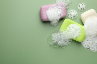 Photo of Soap bars with foam on green background, flat lay. Space for text