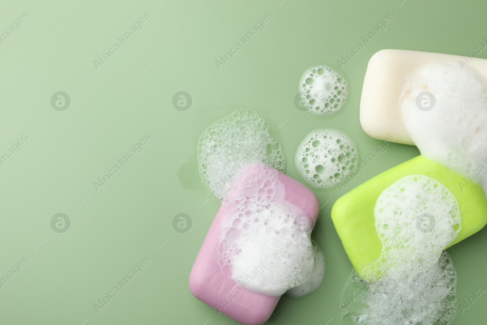 Photo of Soap bars with foam on green background, flat lay. Space for text