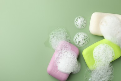 Photo of Soap bars with foam on green background, flat lay. Space for text