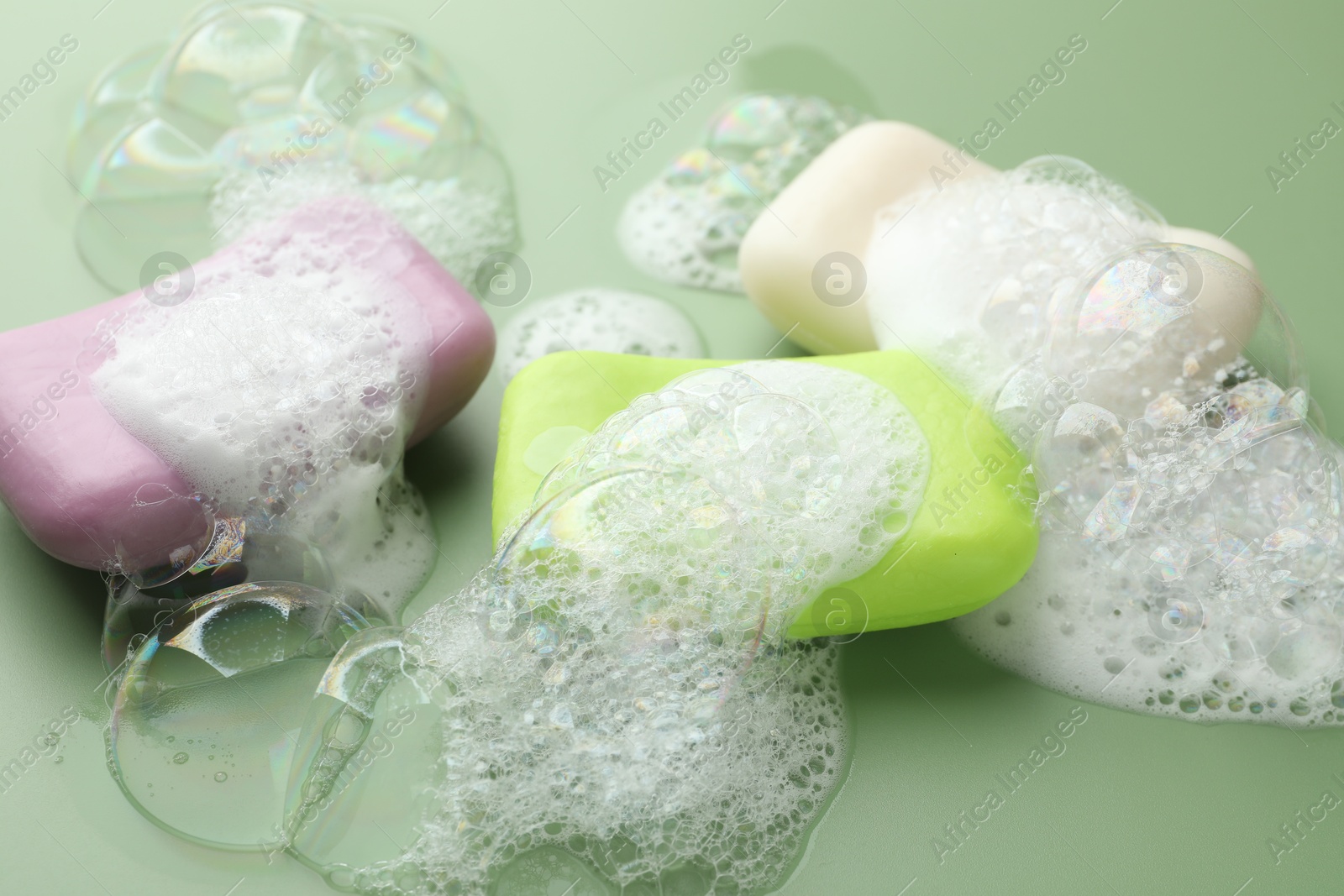 Photo of Soap bars with foam on green background, closeup