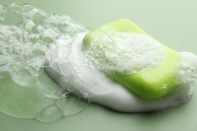 Photo of Soap bar with foam on green background, closeup