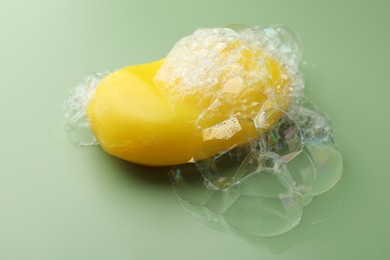 Photo of Soap bar with foam on green background, closeup