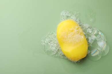 Photo of Soap bar with foam on green background, top view. Space for text