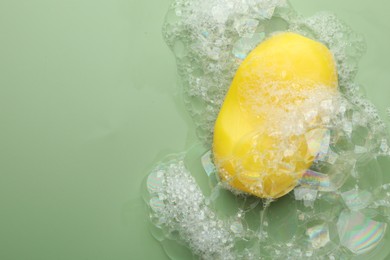 Photo of Soap bar with foam on green background, top view. Space for text