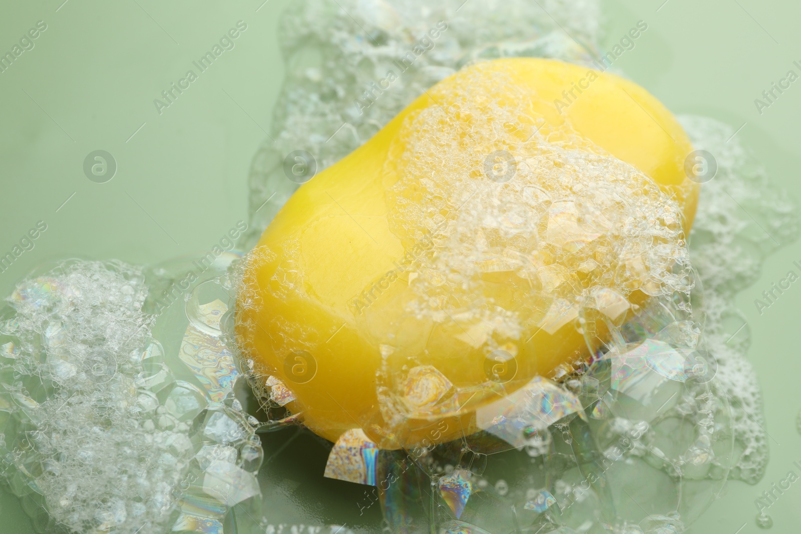 Photo of Soap bar with foam on green background, closeup