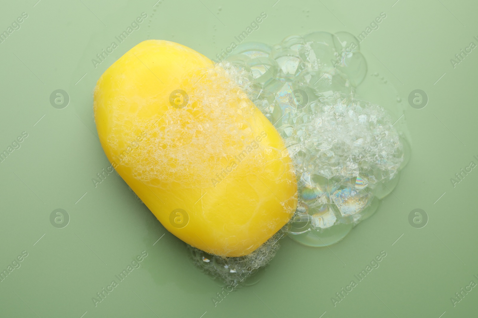 Photo of Soap bar with foam on green background, top view