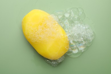 Photo of Soap bar with foam on green background, top view