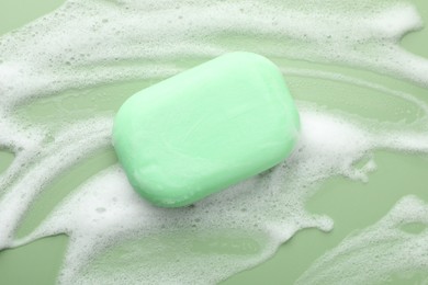 Photo of Soap bar with foam on green background, top view