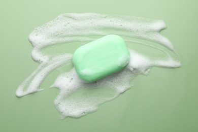 Photo of Soap bar with foam on green background, top view