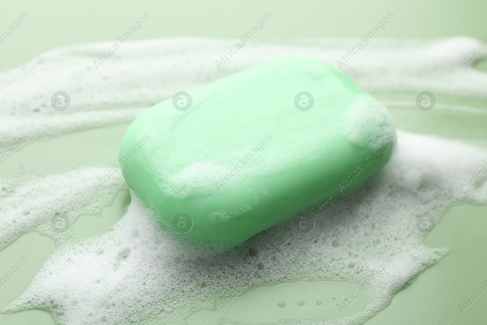 Photo of Soap bar with foam on green background, closeup