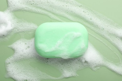 Photo of Soap bar with foam on green background, top view