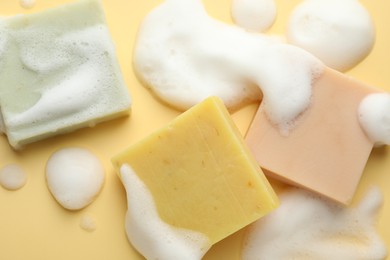 Photo of Soap bars with foam on yellow background, flat lay