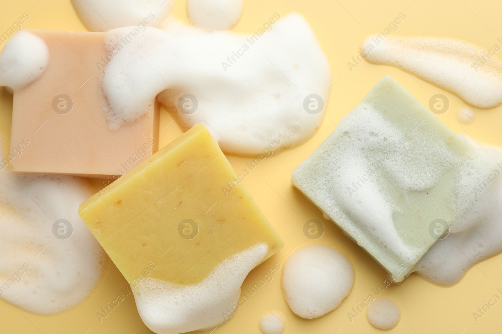 Photo of Soap bars with foam on yellow background, flat lay