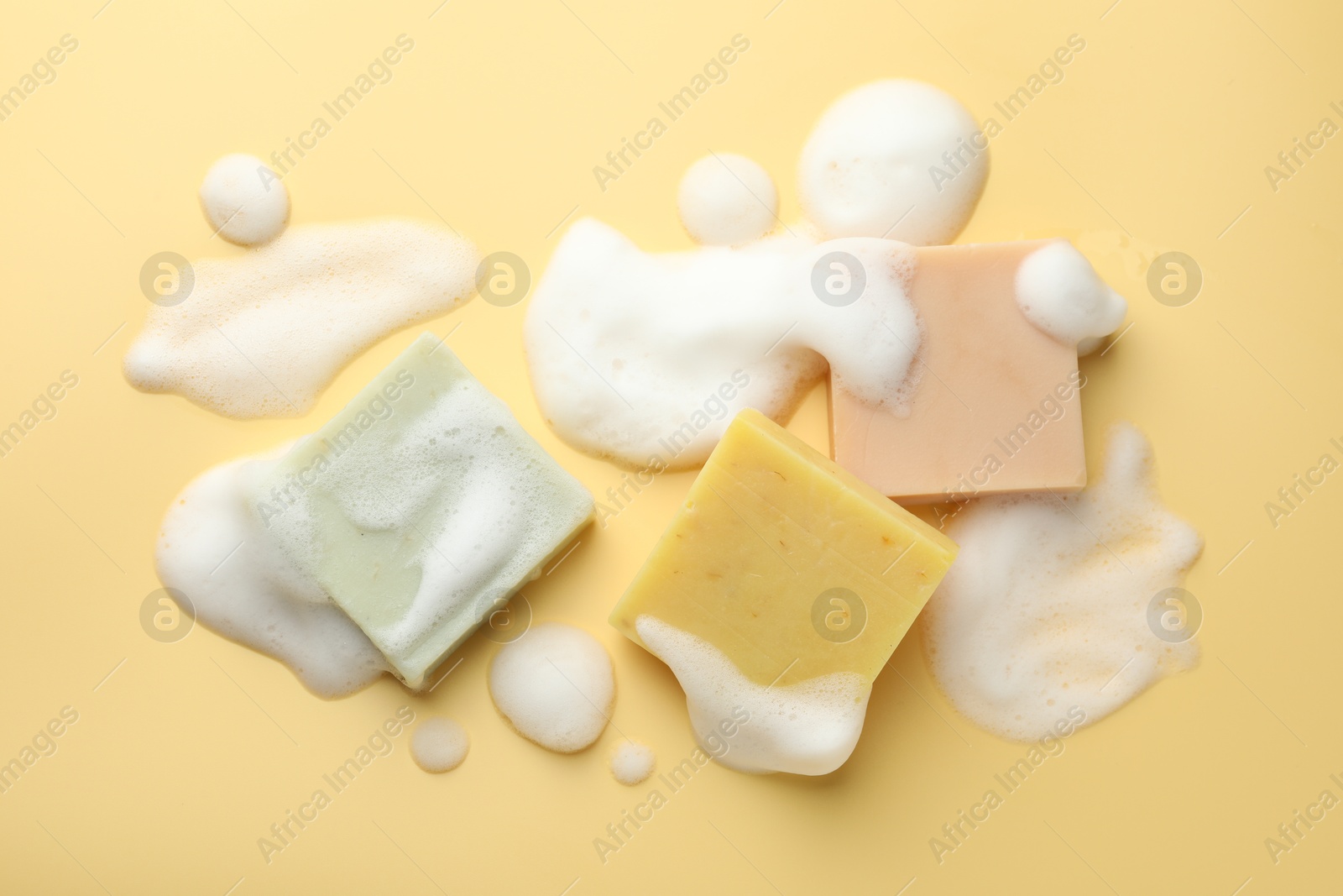 Photo of Soap bars with foam on yellow background, flat lay