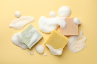 Photo of Soap bars with foam on yellow background, flat lay