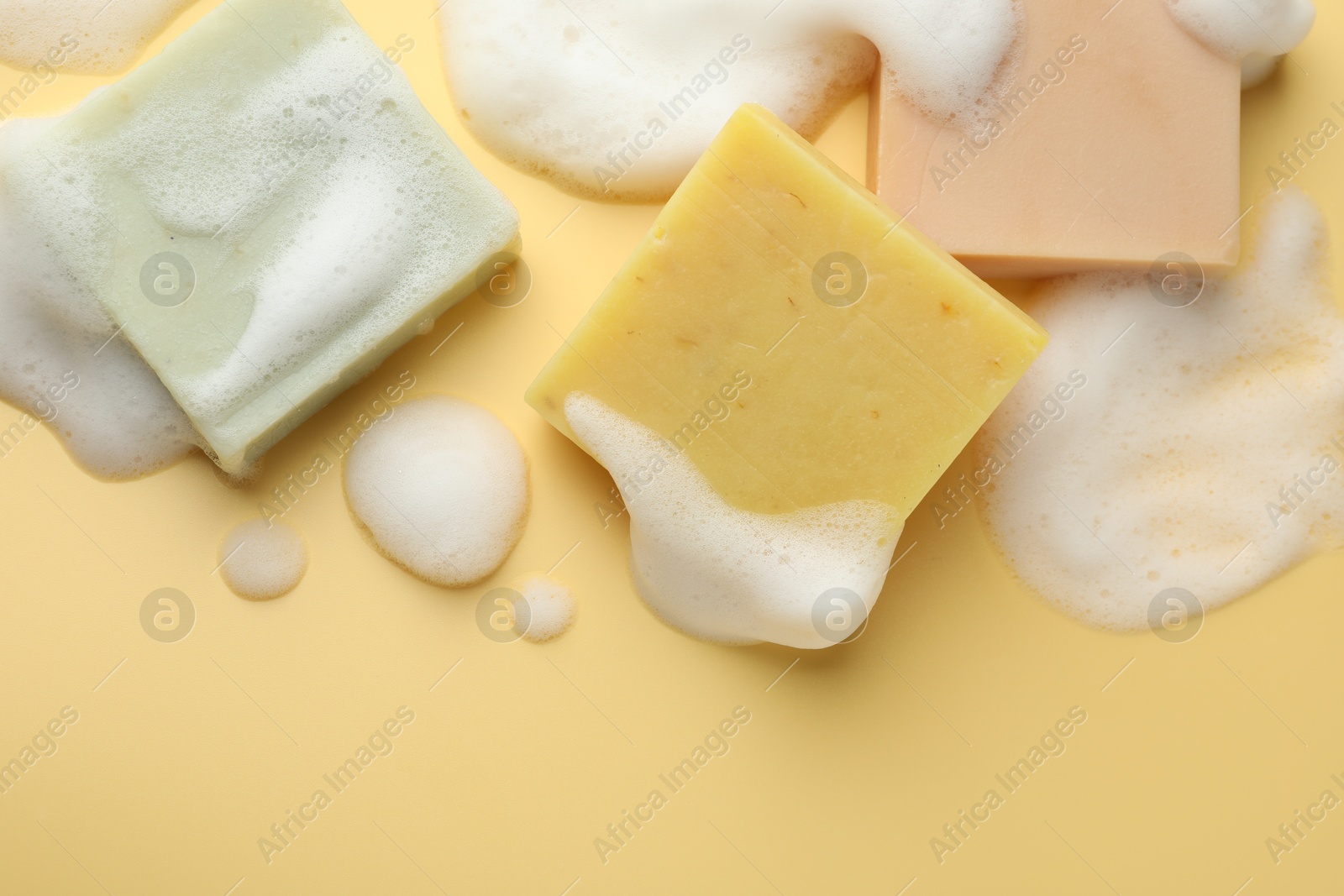 Photo of Soap bars with foam on yellow background, flat lay