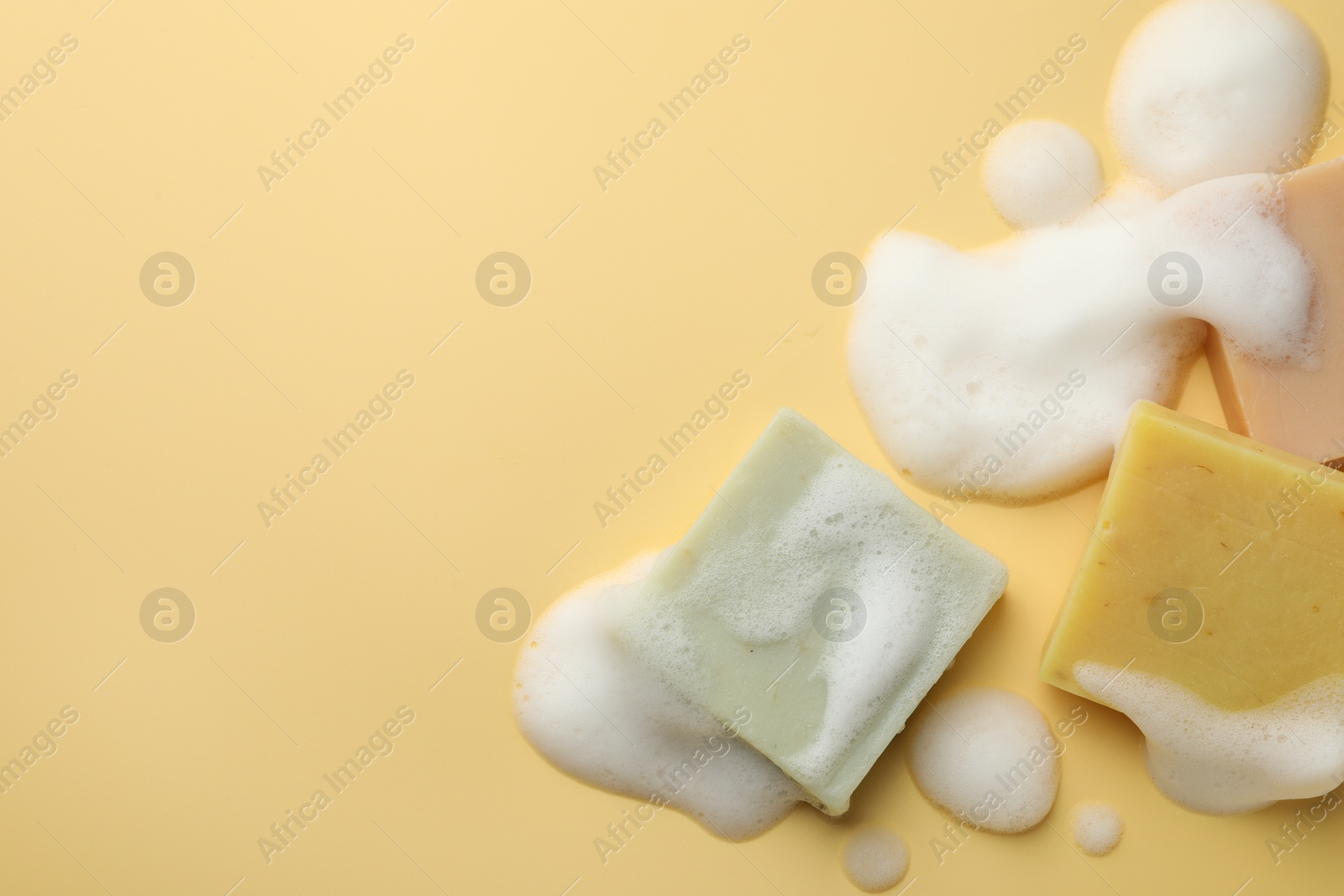 Photo of Soap bars with foam on yellow background, flat lay. Space for text