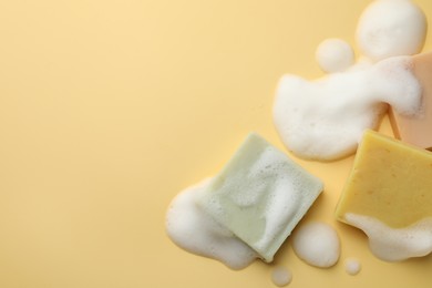 Photo of Soap bars with foam on yellow background, flat lay. Space for text