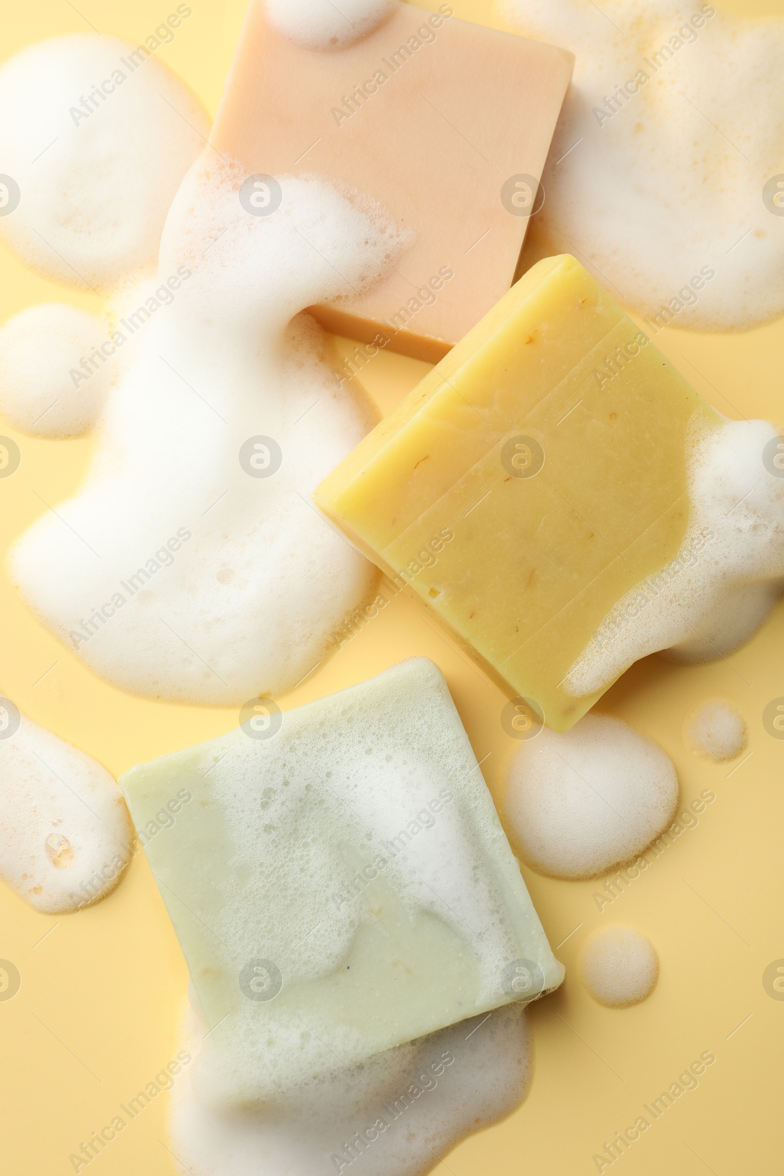 Photo of Soap bars with foam on yellow background, flat lay