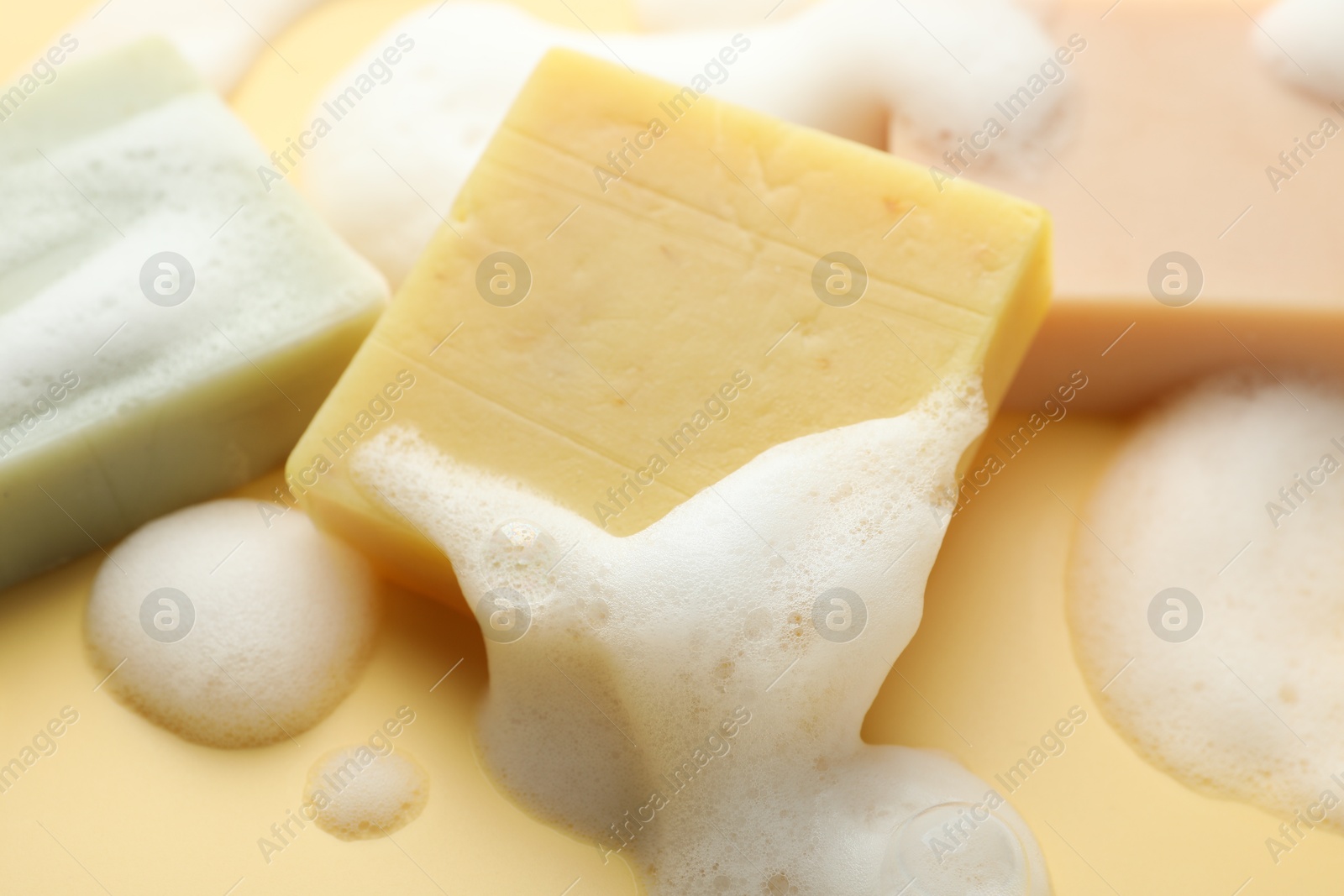 Photo of Soap bars with foam on yellow background, closeup