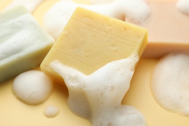 Photo of Soap bars with foam on yellow background, closeup