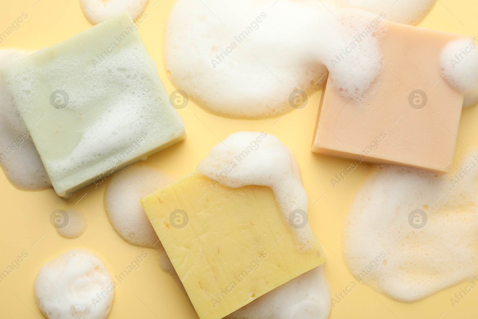 Photo of Soap bars with foam on yellow background, flat lay