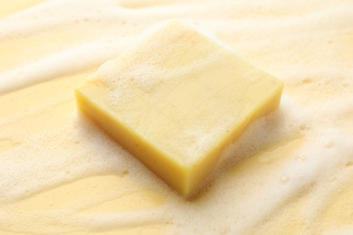 Photo of Soap bar with foam on yellow background, closeup