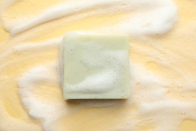 Photo of Soap bar with foam on yellow background, top view