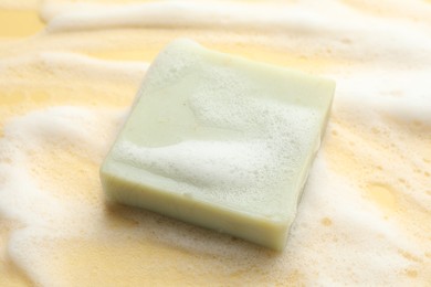 Photo of Soap bar with foam on yellow background, closeup