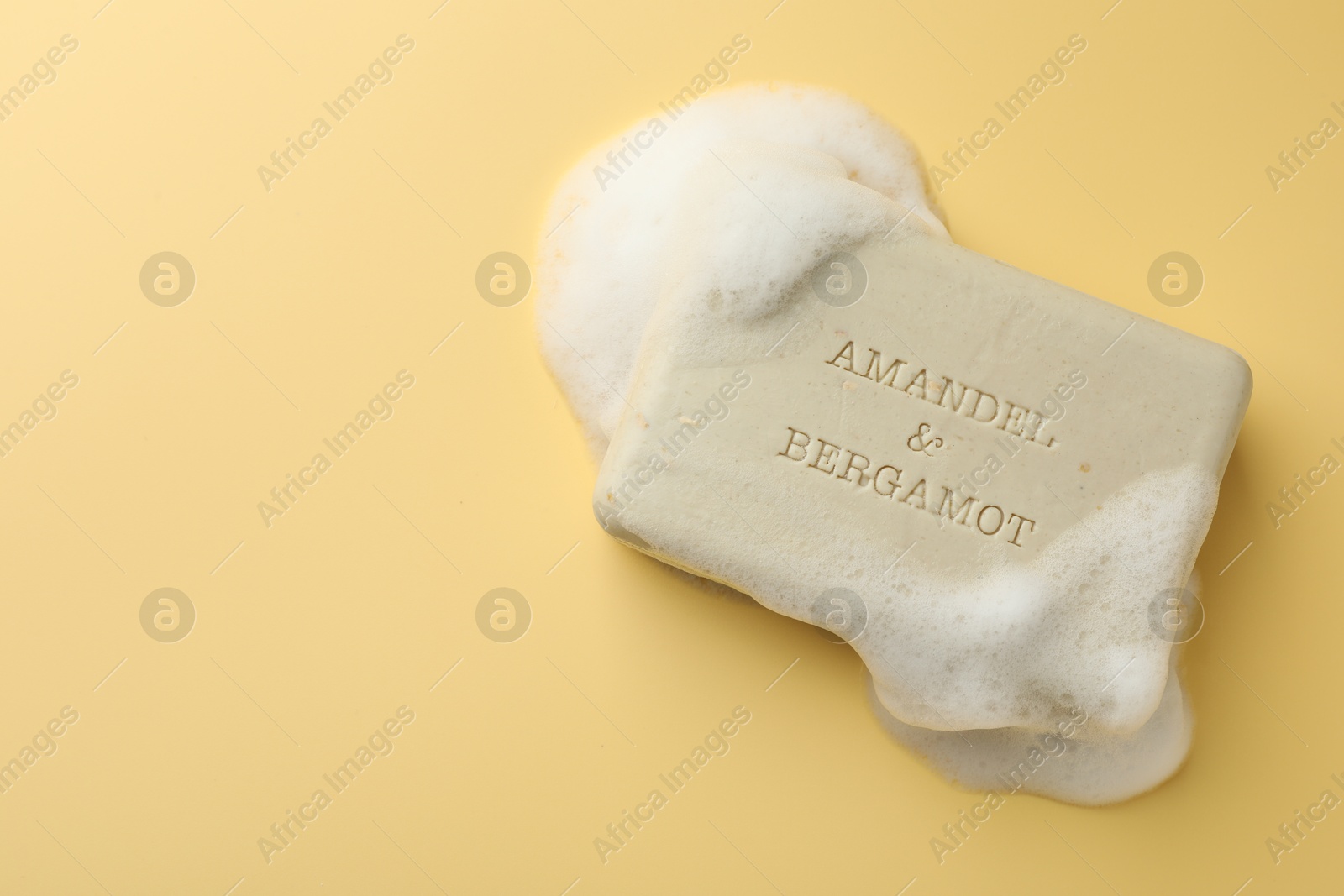 Photo of Soap bar with foam on yellow background, top view. Space for text