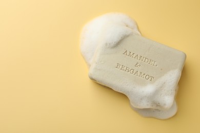 Photo of Soap bar with foam on yellow background, top view. Space for text