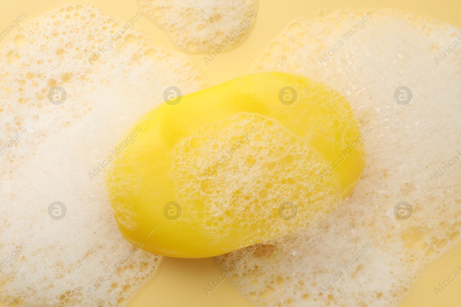 Photo of Soap bar with foam on yellow background, top view