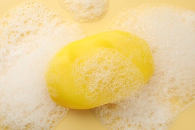 Photo of Soap bar with foam on yellow background, top view