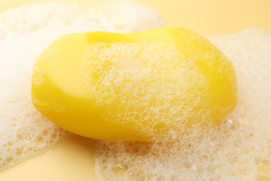 Photo of Soap bar with foam on yellow background, closeup