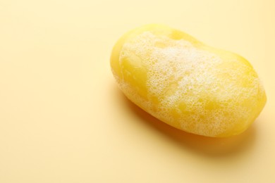 Photo of Soap bar with foam on yellow background, closeup. Space for text